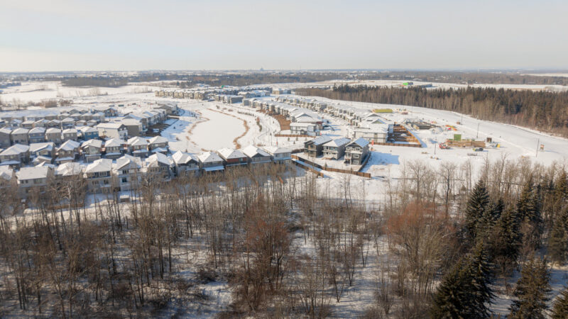 Aerial view of the community showing homes backing onto a snow covered natural area in Kinglet by Big Lake, Edmonton, Alberta.