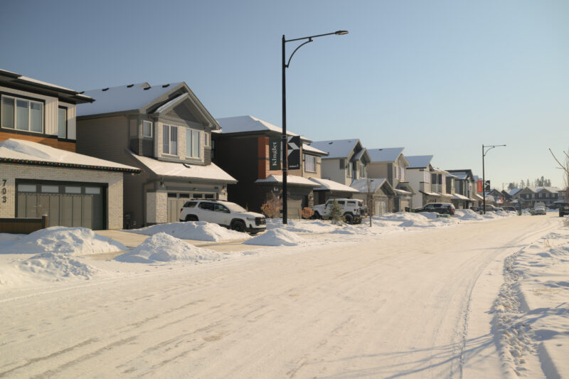 Residential street lined with snow covered front drive homes in Kinglet by Big Lake, Edmonton, Alberta.
