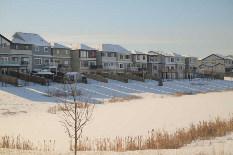 Row of homes overlooking a snow covered storm pond area in Kinglet by Big Lake, Edmonton, Alberta.