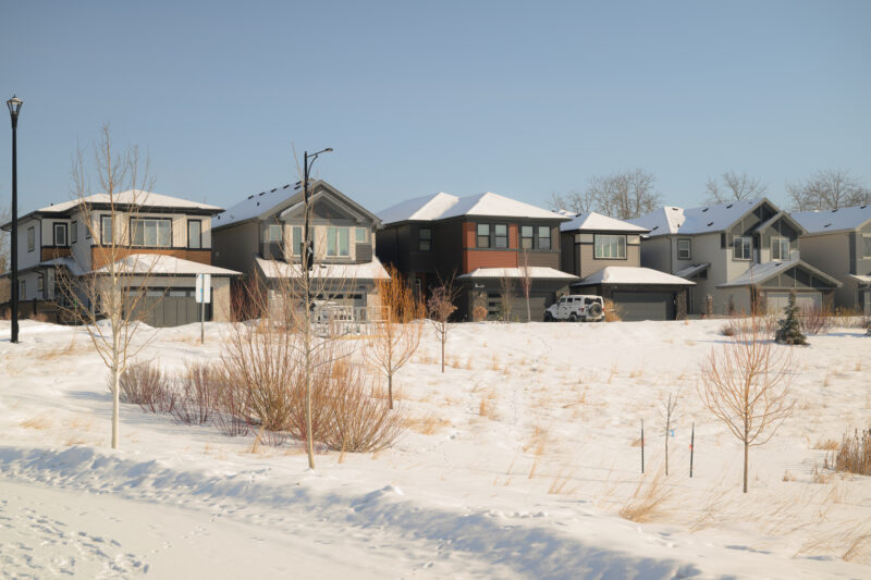 Row of homes backing onto an open snow covered field in Kinglet by Big Lake, Edmonton, Alberta.